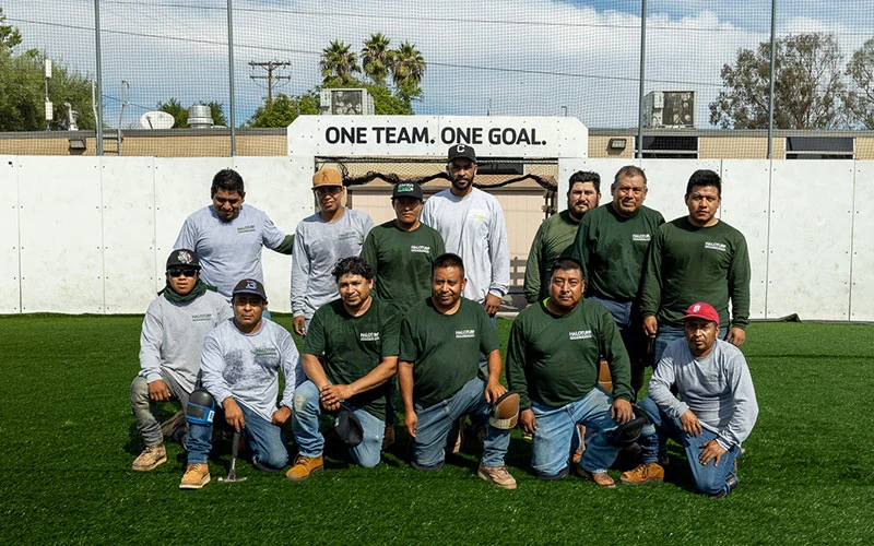 A HaloTurf install crew on a turf field under their One Team One Goal sign